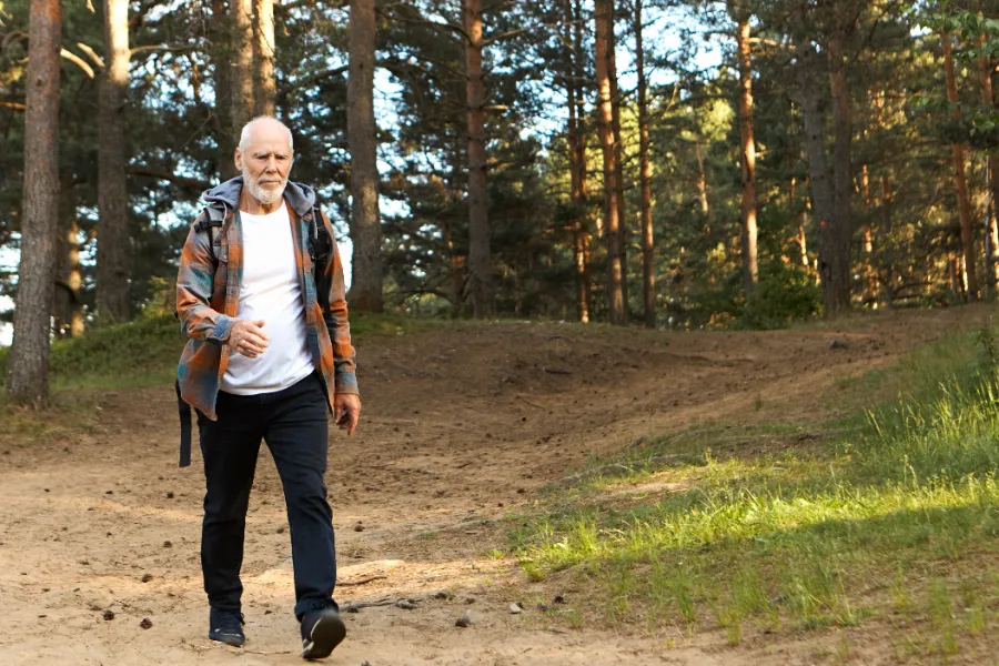 Health activity wellbeing age people concept self determined active bearded european man his sixties walking fast while trekking mountain forest having confident focused look